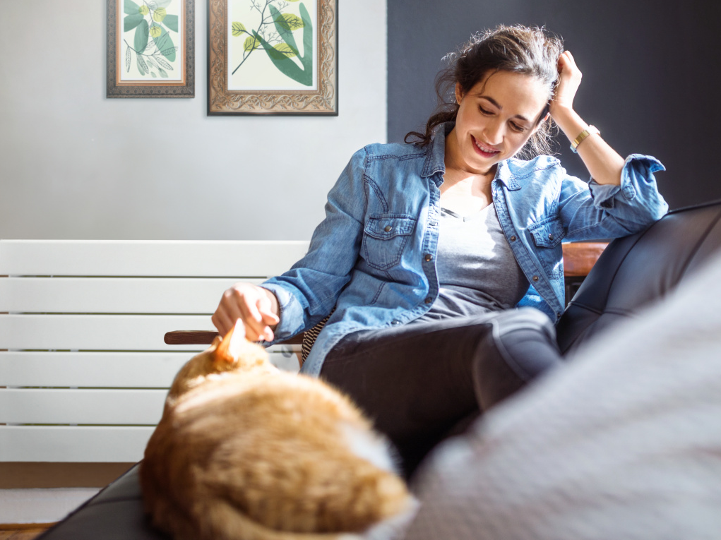 Beautiful young woman relaxing on sofa with her cat in living room.