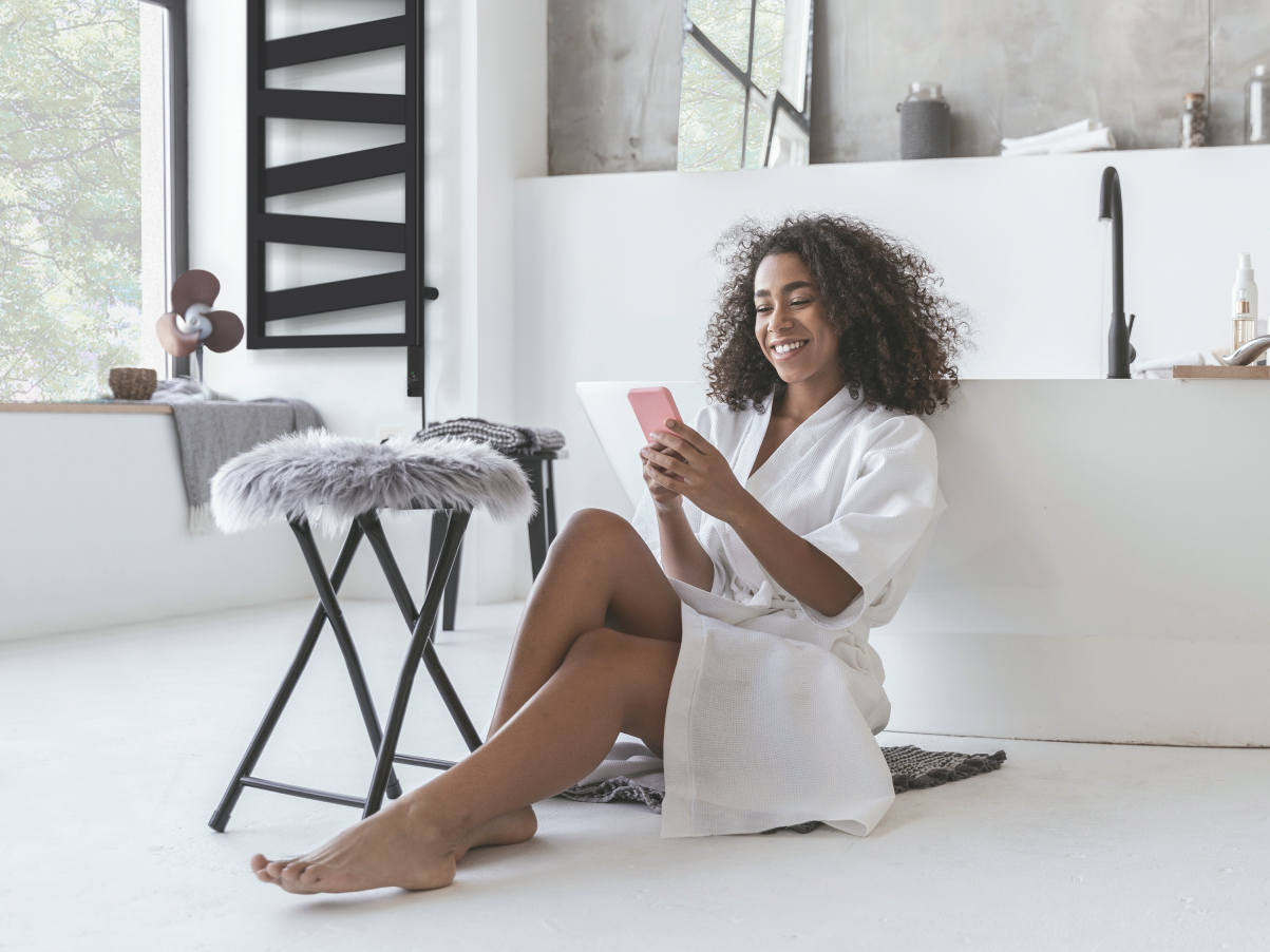 Zehnder_RAD_Ribbon-EL_zeh-nih-keyvisual-300dpi-cmyk Smiling woman sitting in the bathroom on the floor with a smartphone in her hands